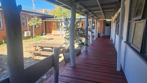 A covered outdoor area with a red wooden floor, benches, and potted plants. - Bunkhouse Motel Cooma (Cooma)