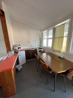 A compact kitchen with a refrigerator, microwave, toaster, and sink. There is a dining table with chairs and a window with curtains. - Bunkhouse Motel Cooma (Cooma)