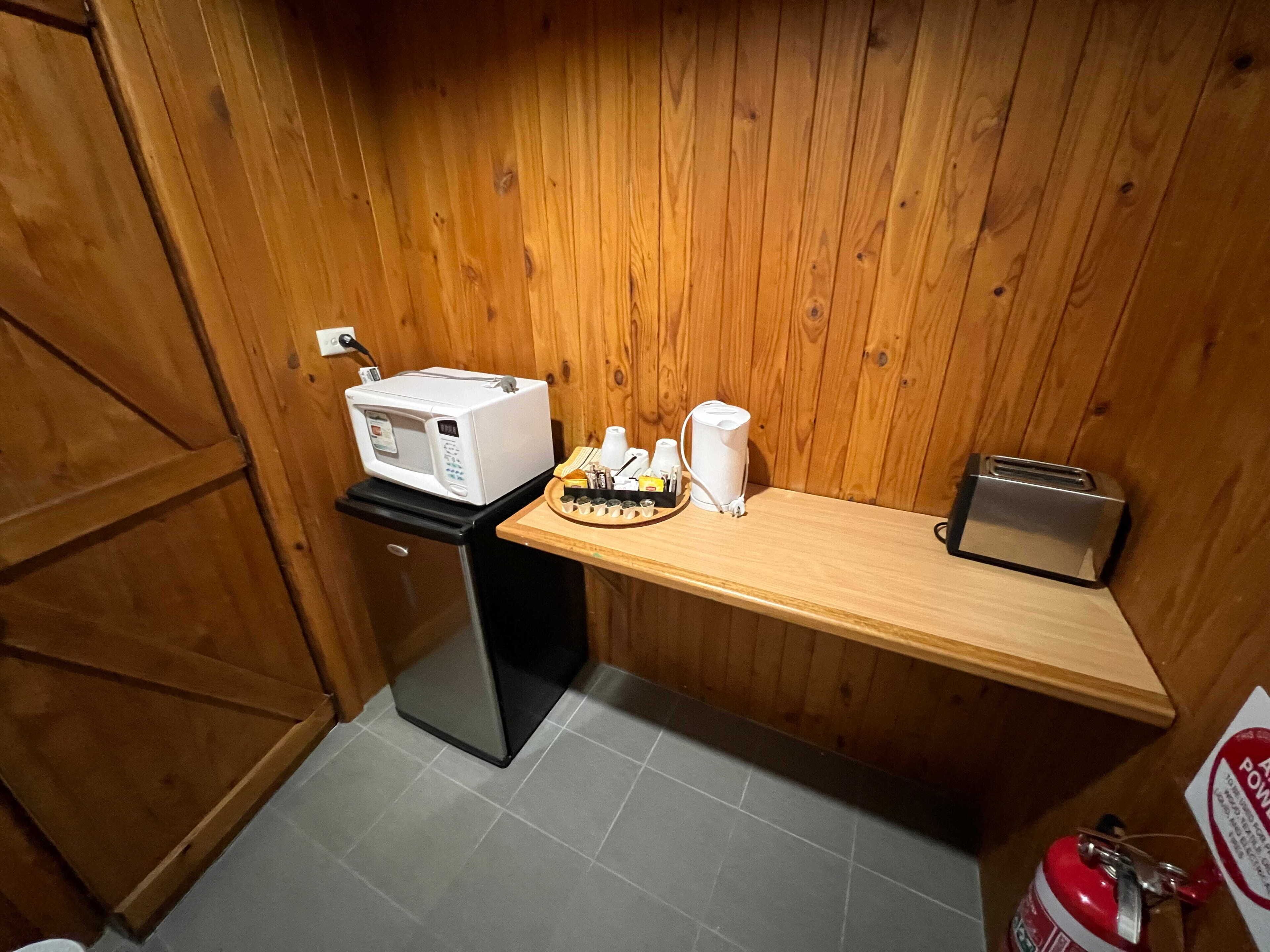 A compact kitchenette with a microwave, toaster, and coffee maker on a wooden countertop.