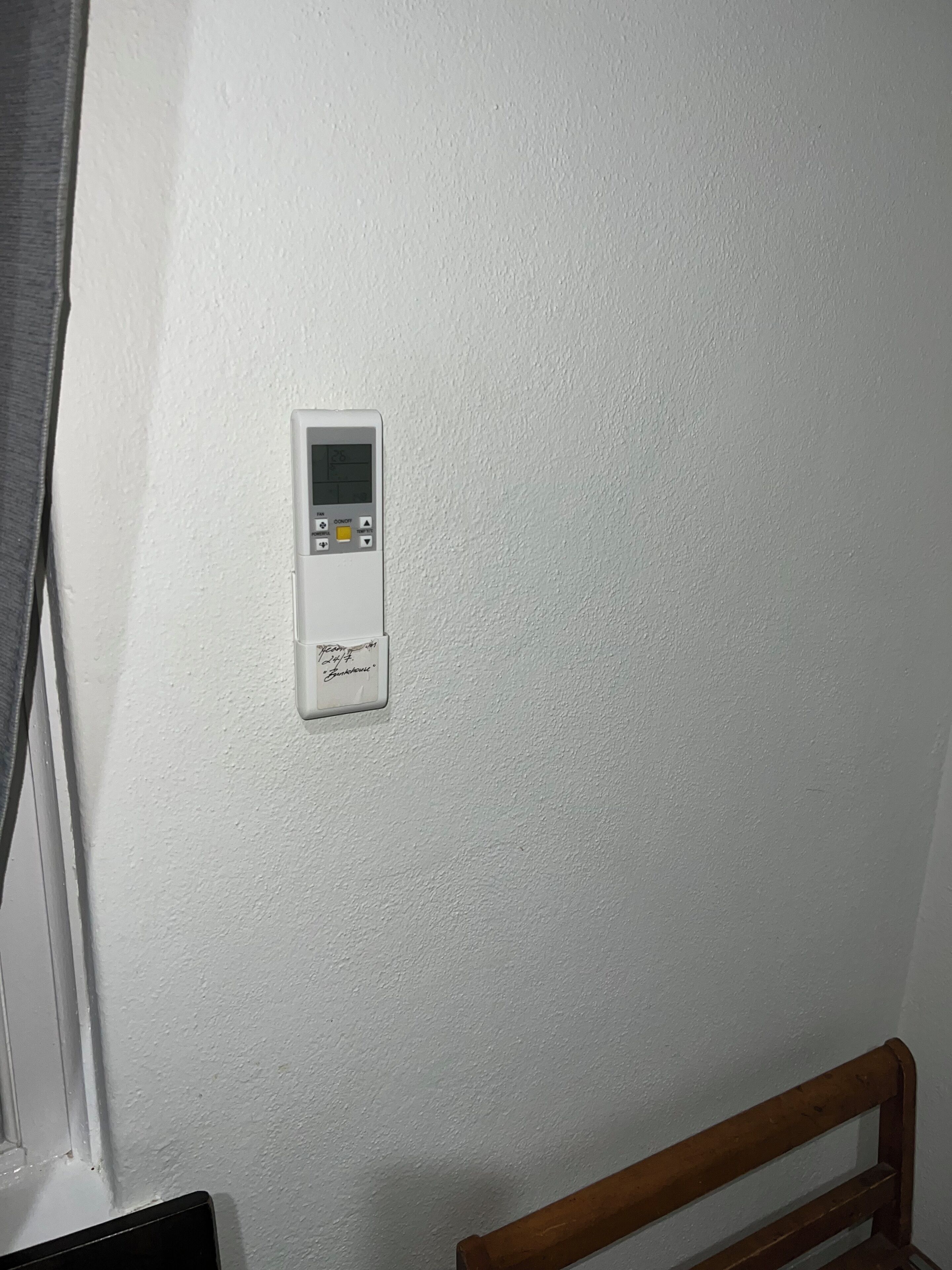 Ein Thermostat an einer weißen Wand, ein Fenster mit Vorhängen und ein hölzernes Kopfteil.