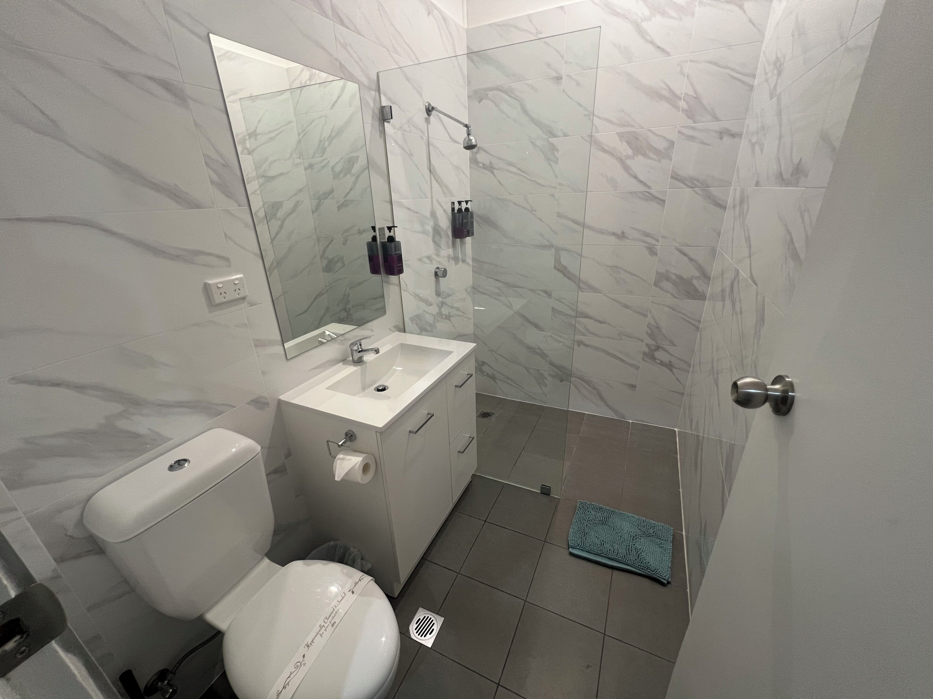 A bathroom with a toilet, sink, mirror, and shower.