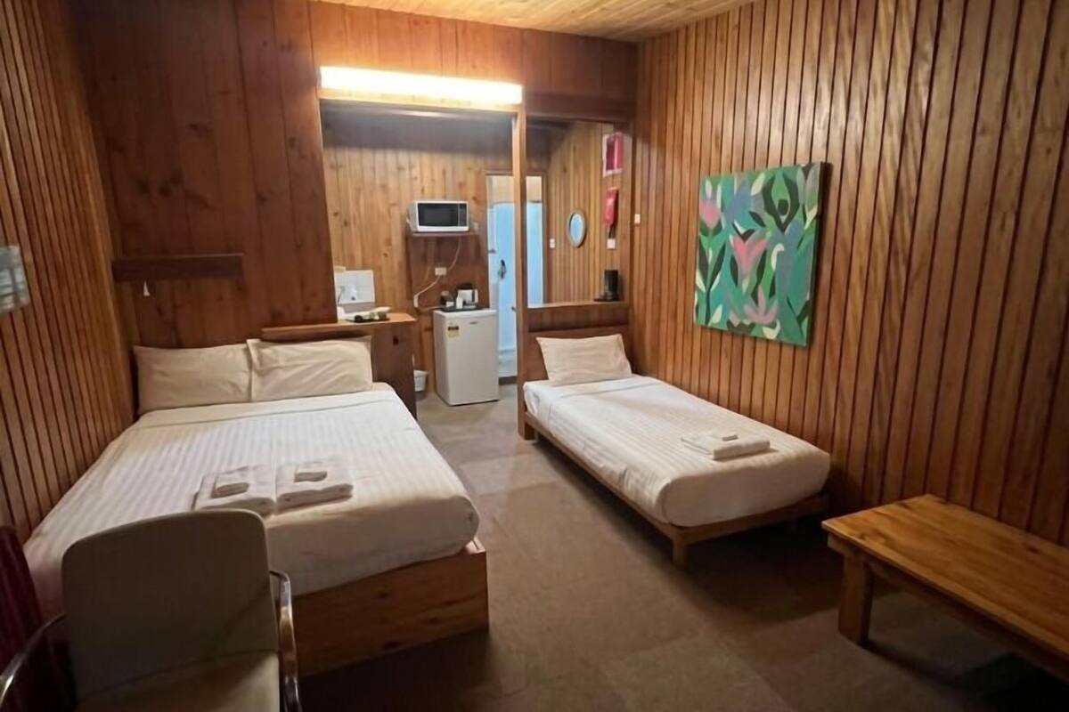 A wooden cabin room with two beds, a small desk, a microwave, and a painting on the wall.