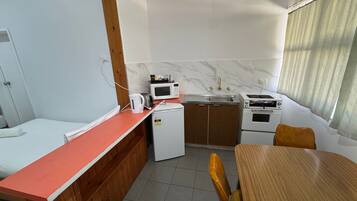 Quarto de hotel compacto com cozinha compacta, uma cama, mesa pequena e janela com cortinas.