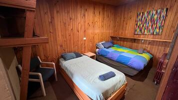 A wooden-paneled room with two beds, a chair, and a colorful artwork on the wall.