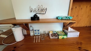 A wooden table with a white wall behind it, a 'hello' sign, a water bottle, a coffee maker, a box of Lipton green tea, a tissue box, and a bag of baby wipes. - Bunkhouse Motel Cooma (Cooma)
