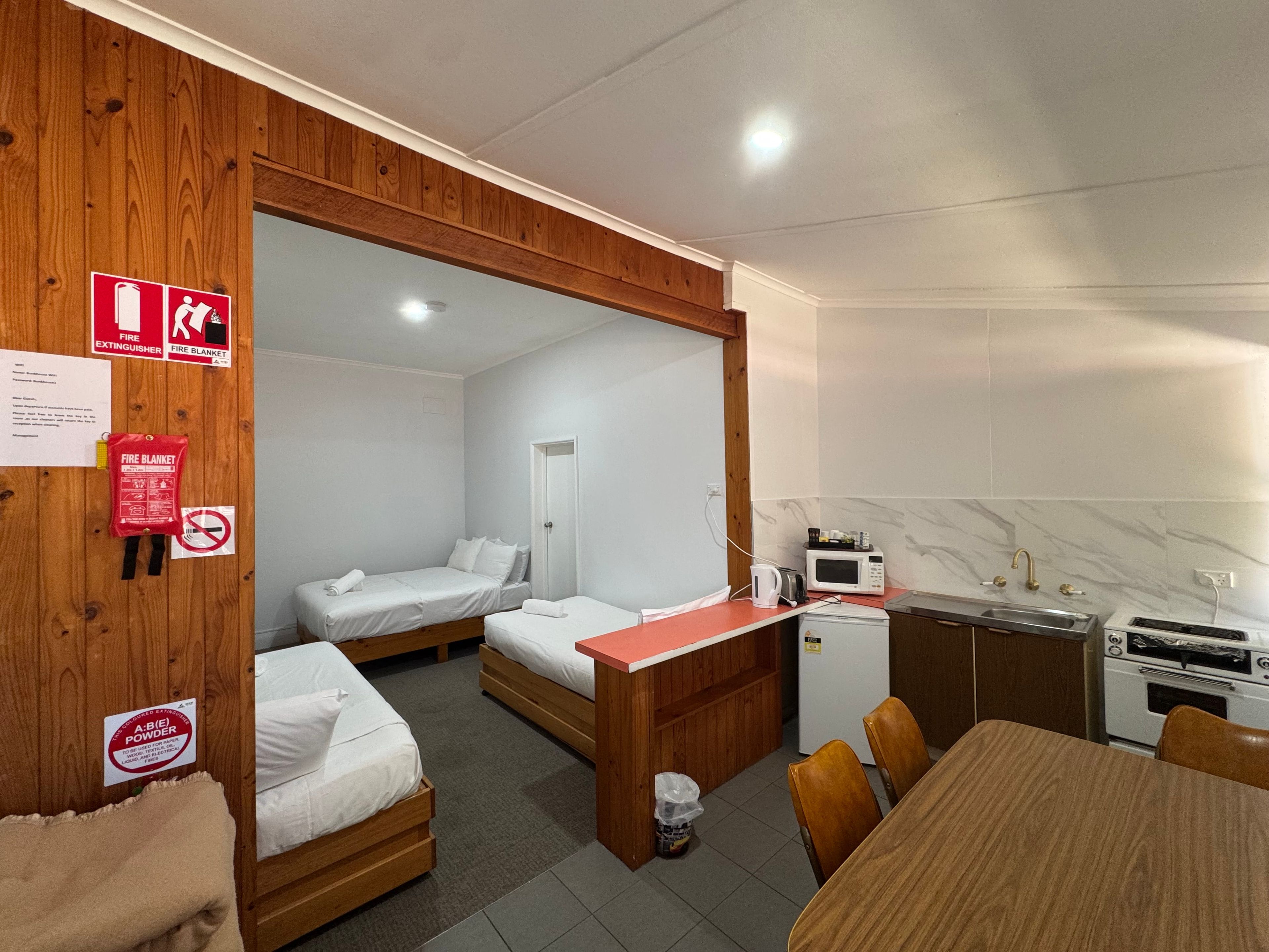 A compact room with two single beds, a kitchenette, a dining table, and a wooden partition.