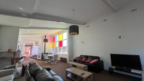 A living room with a black leather sofa, a wooden coffee table, a TV, and a dining area with a table and chairs. - Bunkhouse Motel Cooma (Cooma)