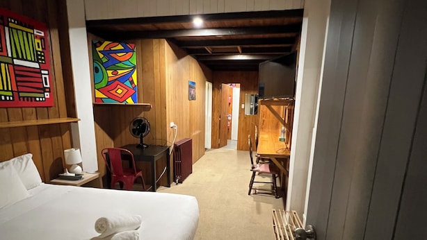 A hotel room with a bed, a desk, a chair, a lamp, and a colorful artwork on the wall. - Bunkhouse Motel Cooma (Cooma)