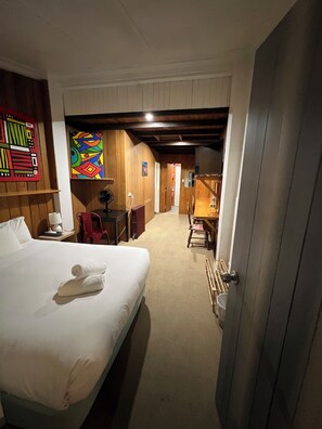 Une chambre d’hôtel avec un lit, un bureau, une chaise, une lampe et une œuvre d’art colorée accrochée au mur.