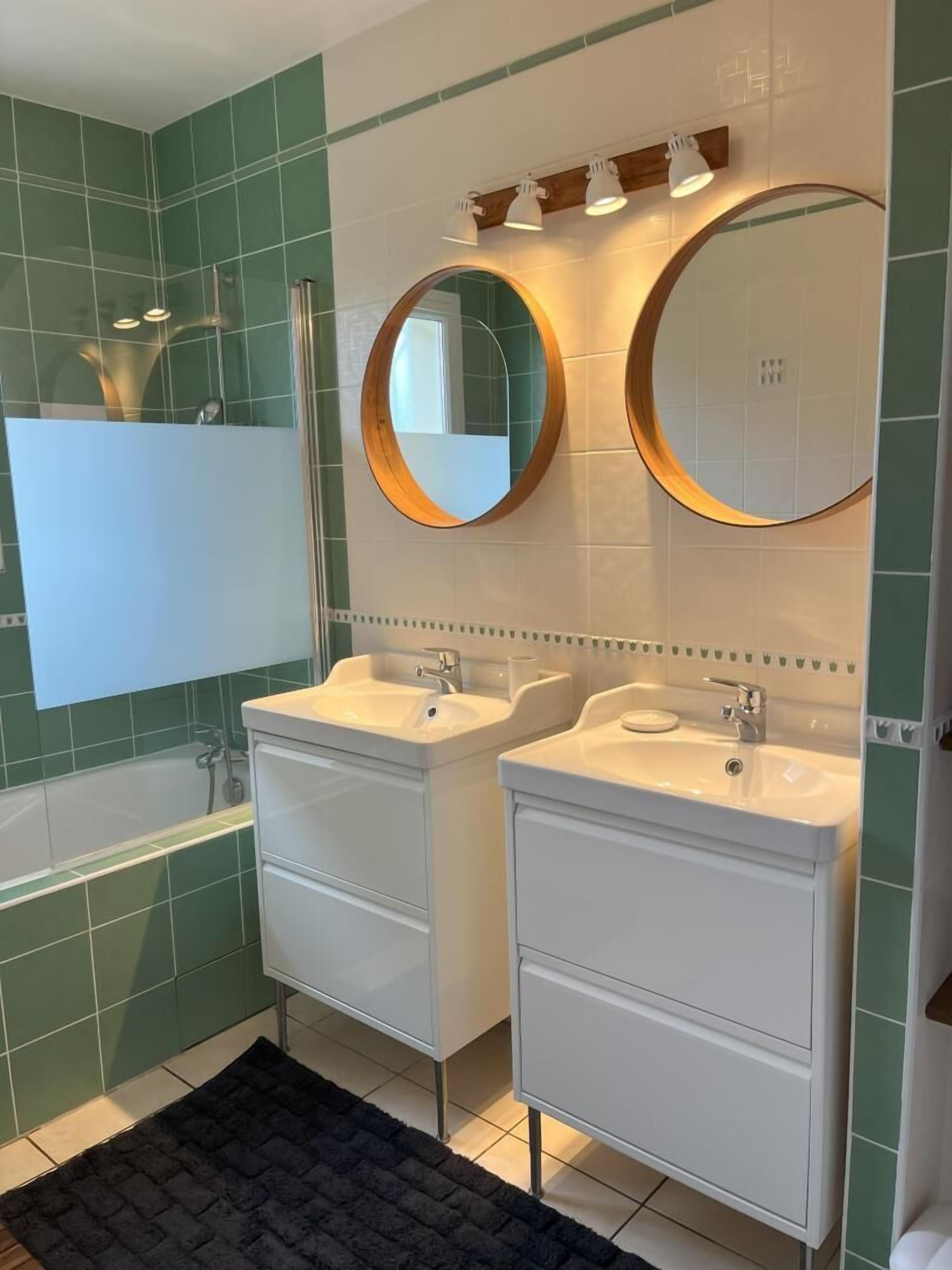A bathroom with two sinks, a bathtub, and two round mirrors.