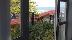 Une fenêtre ouverte donnant sur une plage et un bâtiment au toit rouge.