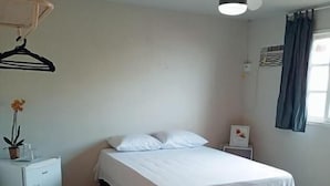 Une chambre à coucher avec un lit, une petite table de chevet, un luminaire suspendu et une fenêtre avec des rideaux.
