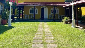 Un bâtiment jaune avec un toit recouvert de tuiles, une entrée centrale et un chemin pavé menant à l’entrée.