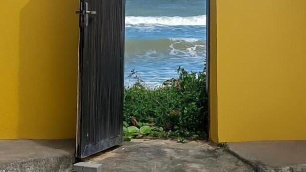 Un mur jaune avec une porte noire qui donne sur l’océan.