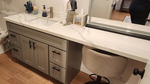 Un baño con inodoro, lavamanos, tocador con cajones y espejo.