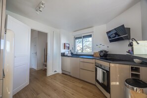 A modern kitchen with a built-in oven, a sink, and a window. - La Maison des Hauts de Touques - Welkeys (Touques)