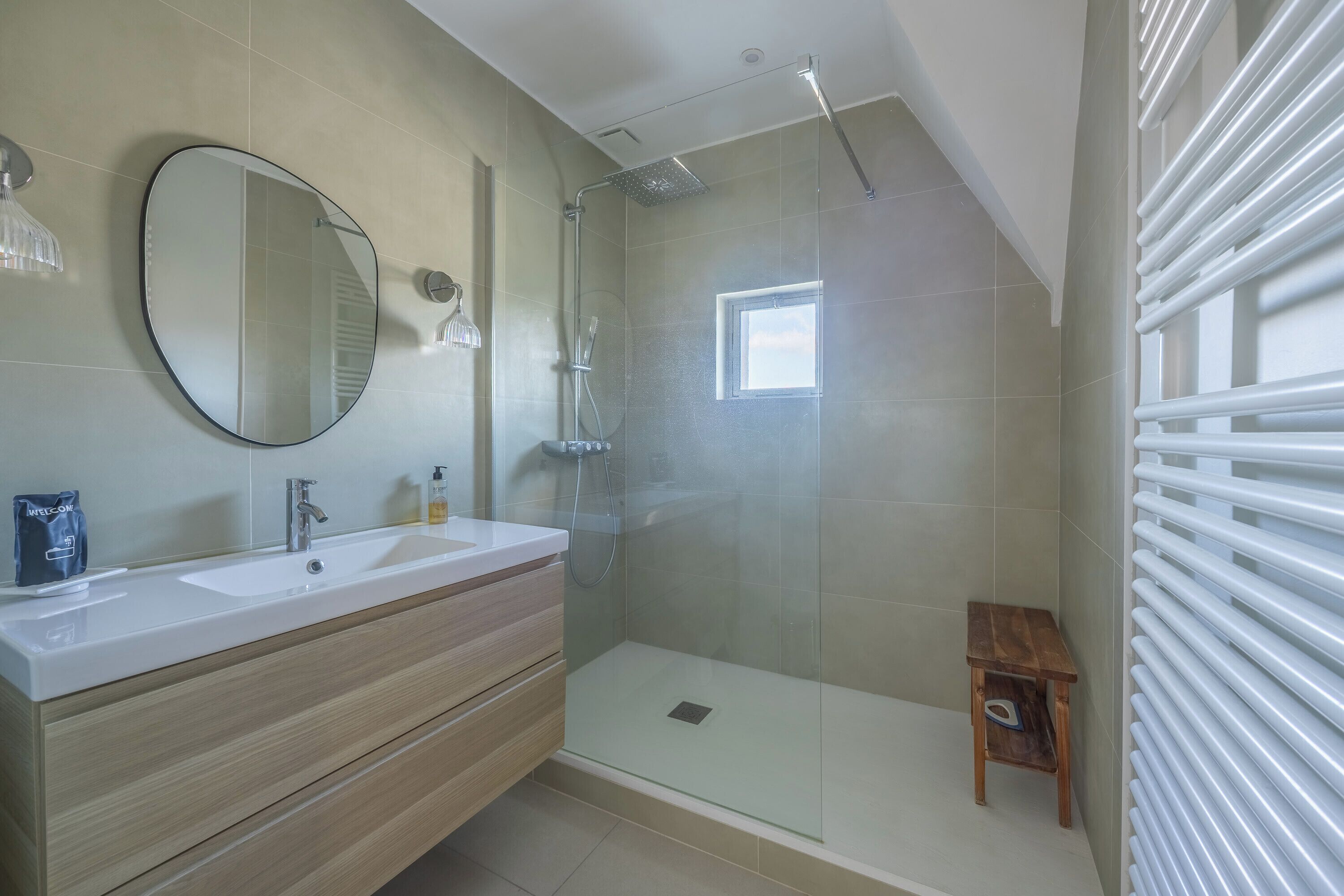 A modern bathroom with a large mirror, a shower enclosure, and a small wooden stool.