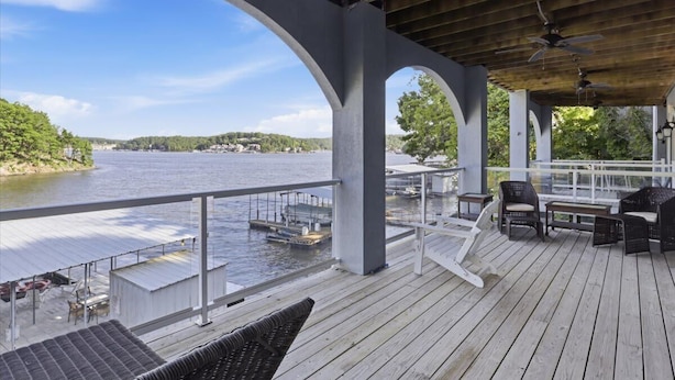 A covered deck with outdoor seating, a view of a lake, and docked boats.