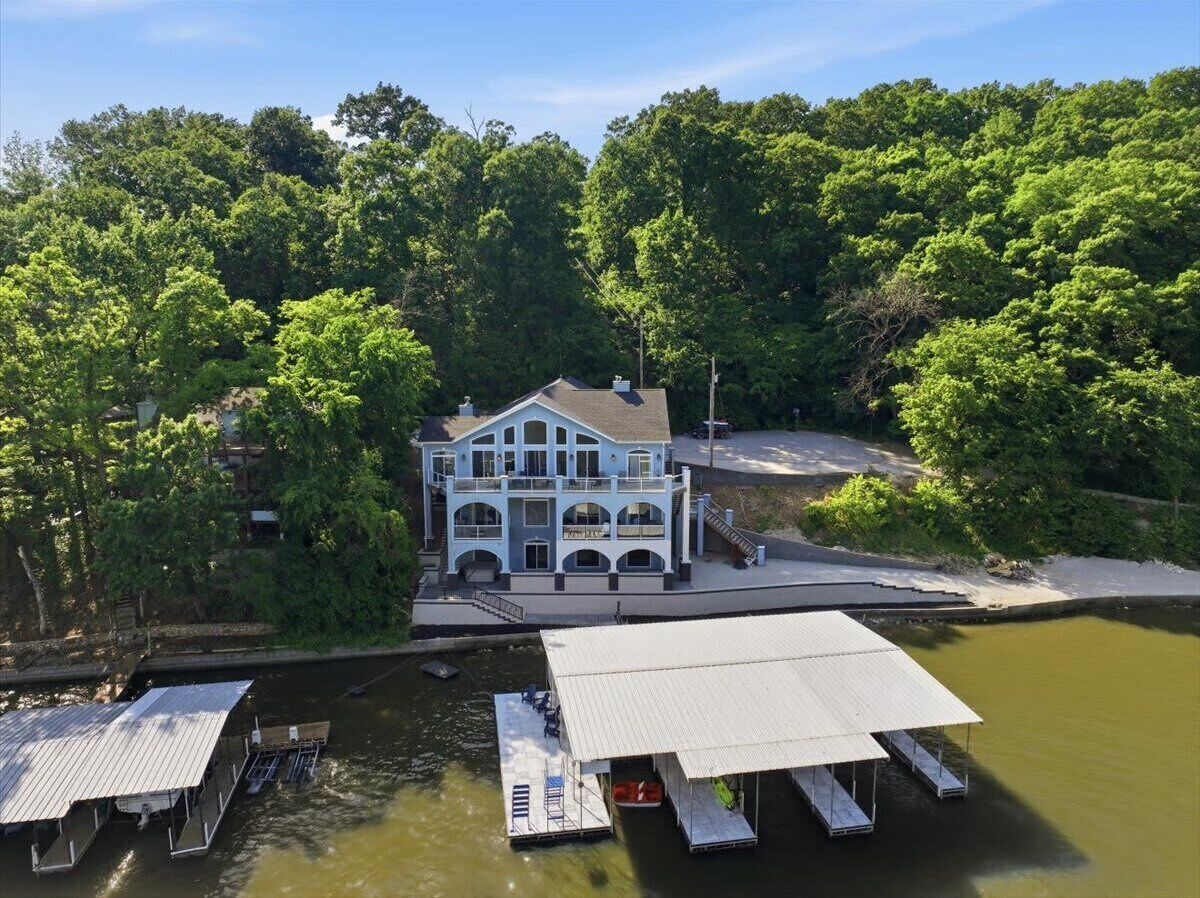 Aerial view of a waterfront vacation rental property with private shoreline, outdoor spaces, and surrounding wooded landscape.