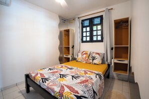 A bedroom with a bed, a window with curtains, and built-in wardrobes. - Modern F3 apartment in the heart of the Baie des Mulets peninsula (Le Vauclin)