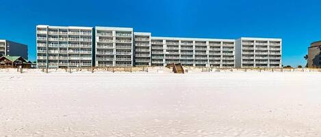 A beachfront hotel with multiple floors, a sandy beach in the foreground, and a clear blue sky.