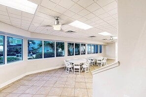 Ein geräumiges Zimmer mit großen Fenstern, einem Deckenventilator und einem Fliesenboden.