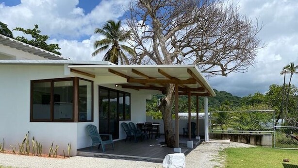 A modern house with a covered patio, a lawn, and a view of the surrounding landscape. - Lovely Caribbean Apartment with AC + Wifi + BBQ + Beach + Kitchen + Parking (Puerto Lindo)