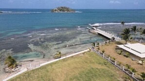 A coastal view with a pier, clear waters, and a small island in the distance. - Lovely Caribbean Apartment with AC + Wifi + BBQ + Beach + Kitchen + Parking (Puerto Lindo)
