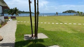 A grassy area with a pathway leading to a building, palm trees, and a view of the sea. - Lovely Caribbean Apartment with AC + Wifi + BBQ + Beach + Kitchen + Parking (Puerto Lindo)