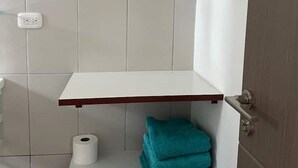 A bathroom with white tiled walls, a white shelf, and a teal towel. - Lovely Caribbean Apartment with AC + Wifi + BBQ + Beach + Kitchen + Parking (Puerto Lindo)