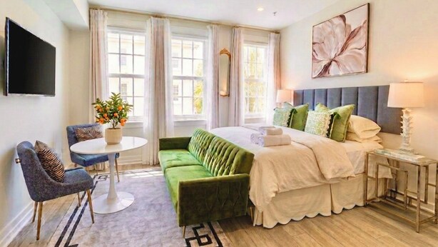 A hotel room with a bed, a desk, a chair, a plant, and a painting. - The Green Room - Serene Poolview Studio with Parking Spot and 24x7 Front Desk (Palm Beach)