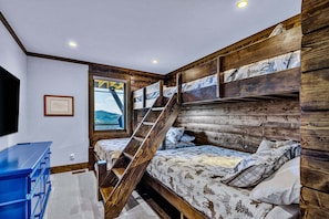 Een slaapkamer met een stapelbed, een houten trap, een groot raam en een blauwe dressoir.