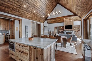 A spacious kitchen with a large island, wooden ceiling, and a stone fireplace. - Skyrise at Eagles Nest - Layered mountain views, luxury home (Banner Elk)