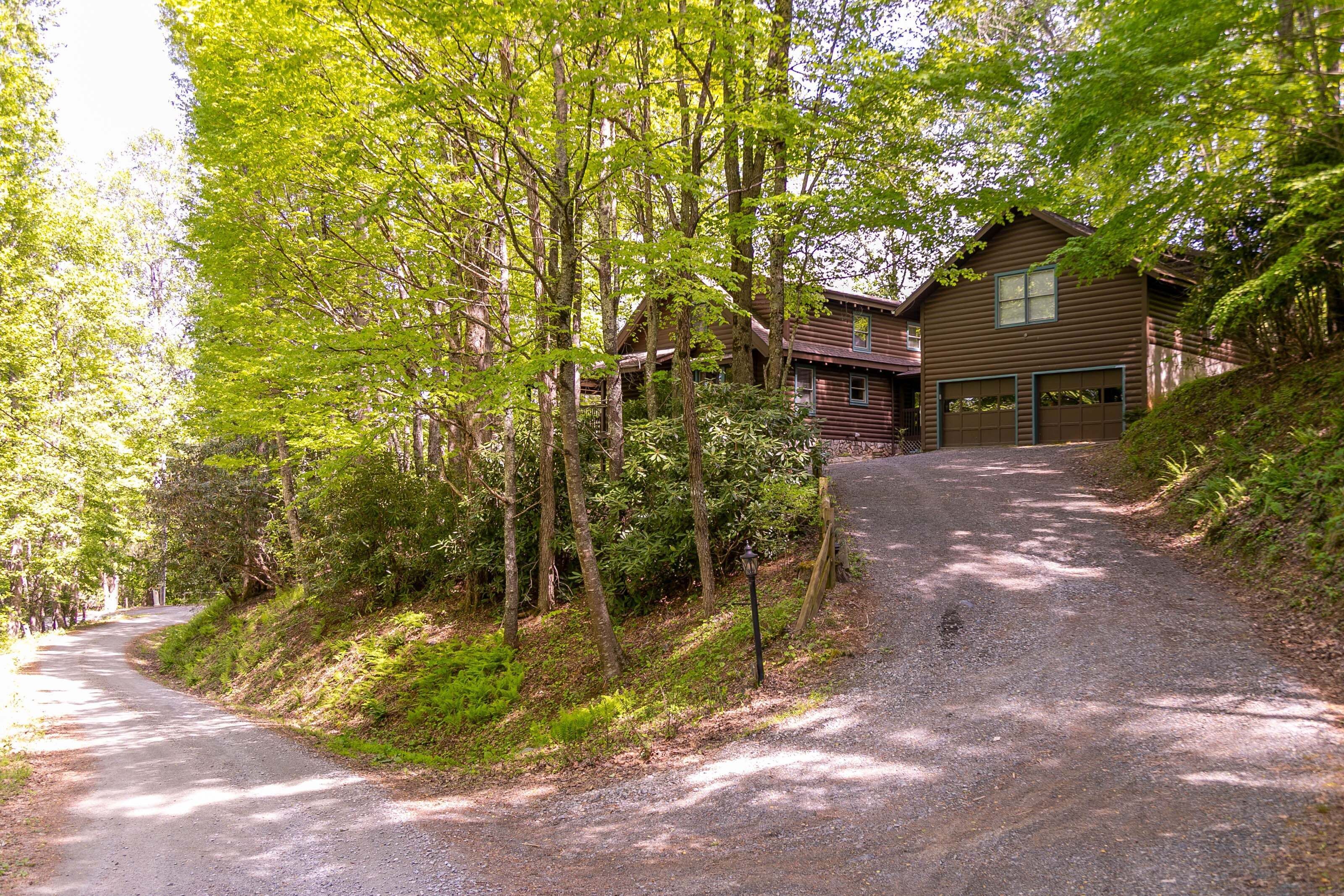 A wooden cabin with a gravel driveway, surrounded by dense forest.
