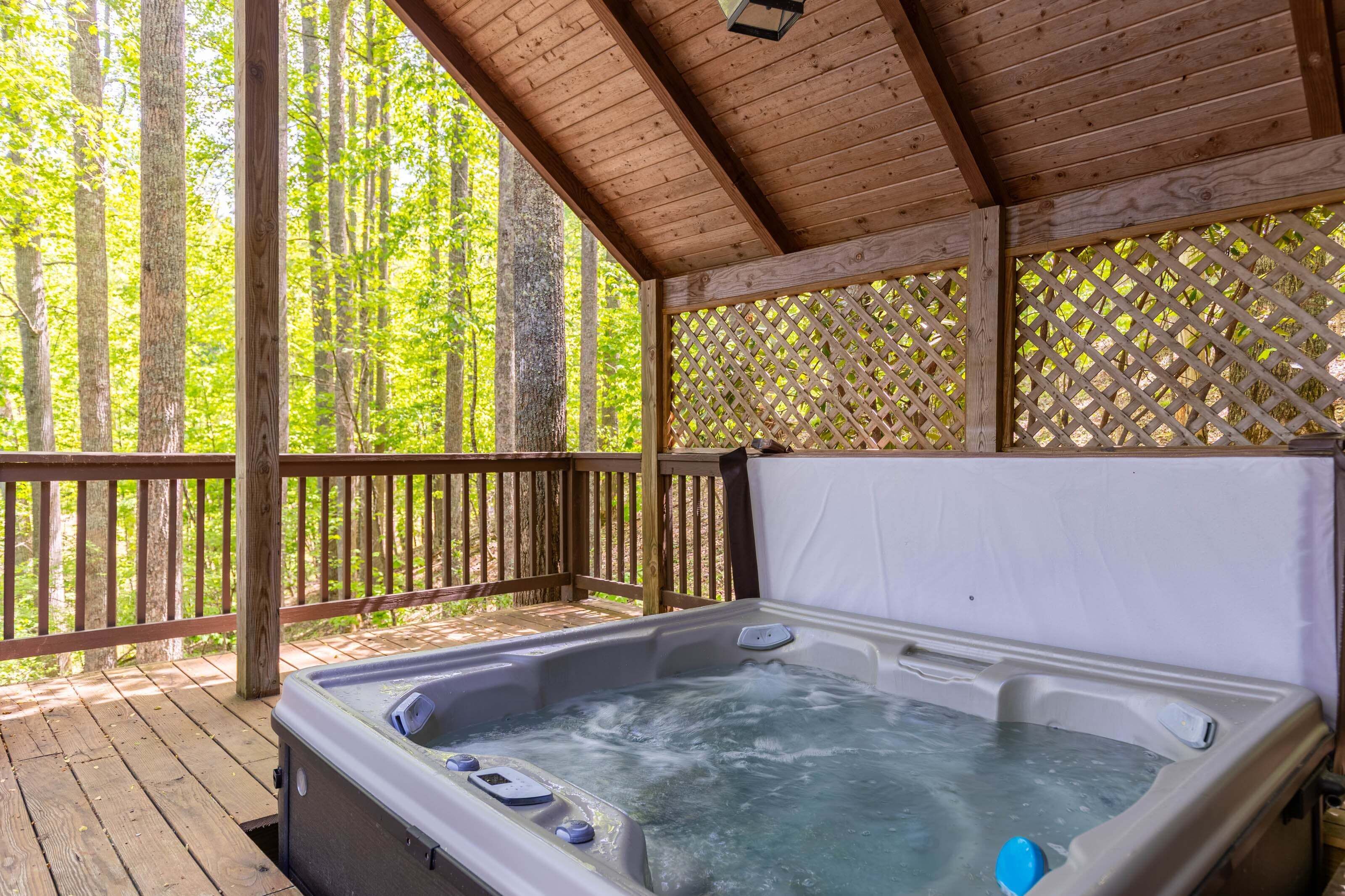 Un jacuzzi debajo de una terraza de madera con un cerramiento de celosía y árboles al fondo.