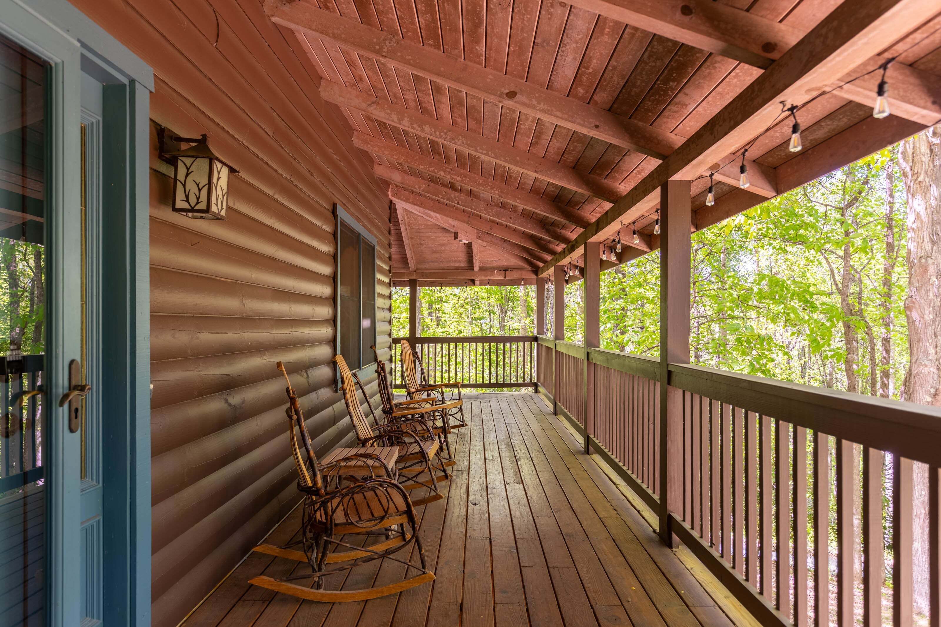 A wooden porch with rocking chairs, a wooden ceiling, and a view of trees.