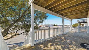 A wooden deck with a white railing, overlooking a parking area and buildings in the background. - Perfect Break | Private Pool and Hot Tub | Less than 1,000 ft to the Beach! (Kill Devil Hills)