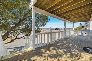 Une terrasse en bois avec une balustrade blanche, donnant sur un parking et sur des bâtiments situés au loin.