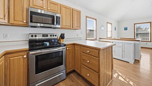 A modern kitchen with wooden cabinets, stainless steel appliances, and a large island. - Perfect Break | Private Pool and Hot Tub | Less than 1,000 ft to the Beach! (Kill Devil Hills)
