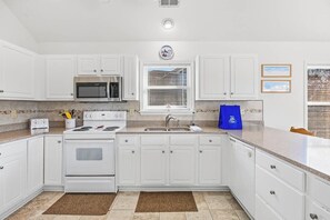 A kitchen with white cabinets, a microwave, a stove, a sink, and a clock on the wall. - Sunny Lagoon | Walk to Beach & Sound | Hot Tub and Dog Friendly (Duck)