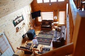 Ein gemütliches Blockhäuschen-Interieur mit Fernseher, Holzwänden, einem gemusterten Teppich und einer Couch.