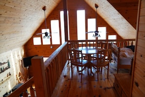 Eine Holzhütte mit Schlafzimmer auf dem Dachboden, einem Essbereich mit rundem Tisch und Stühlen sowie einem Balkon mit Geländer.
