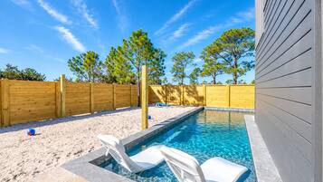 A swimming pool with two lounge chairs, a wooden fence, and trees in the background.