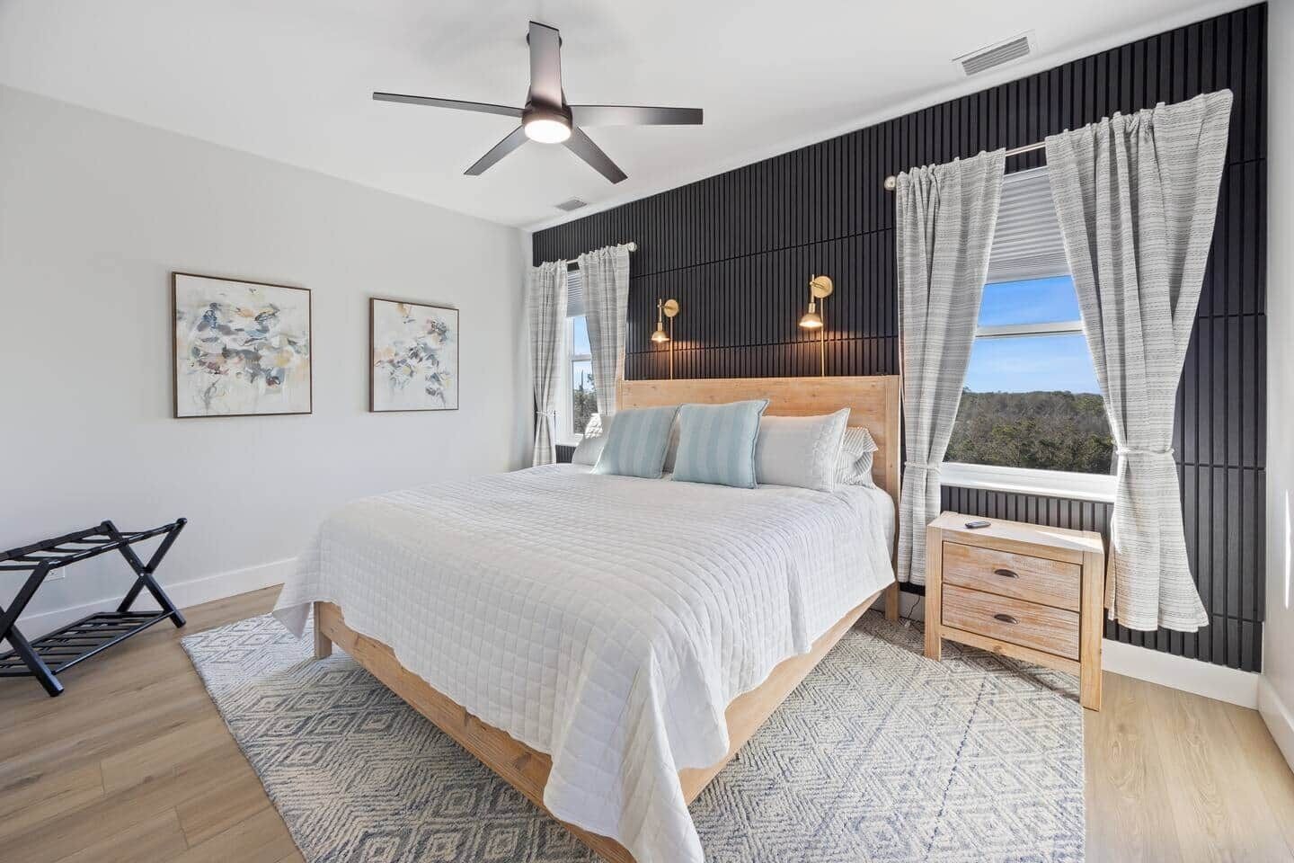 A modern bedroom with a large bed, a ceiling fan, a nightstand, and a window with curtains.