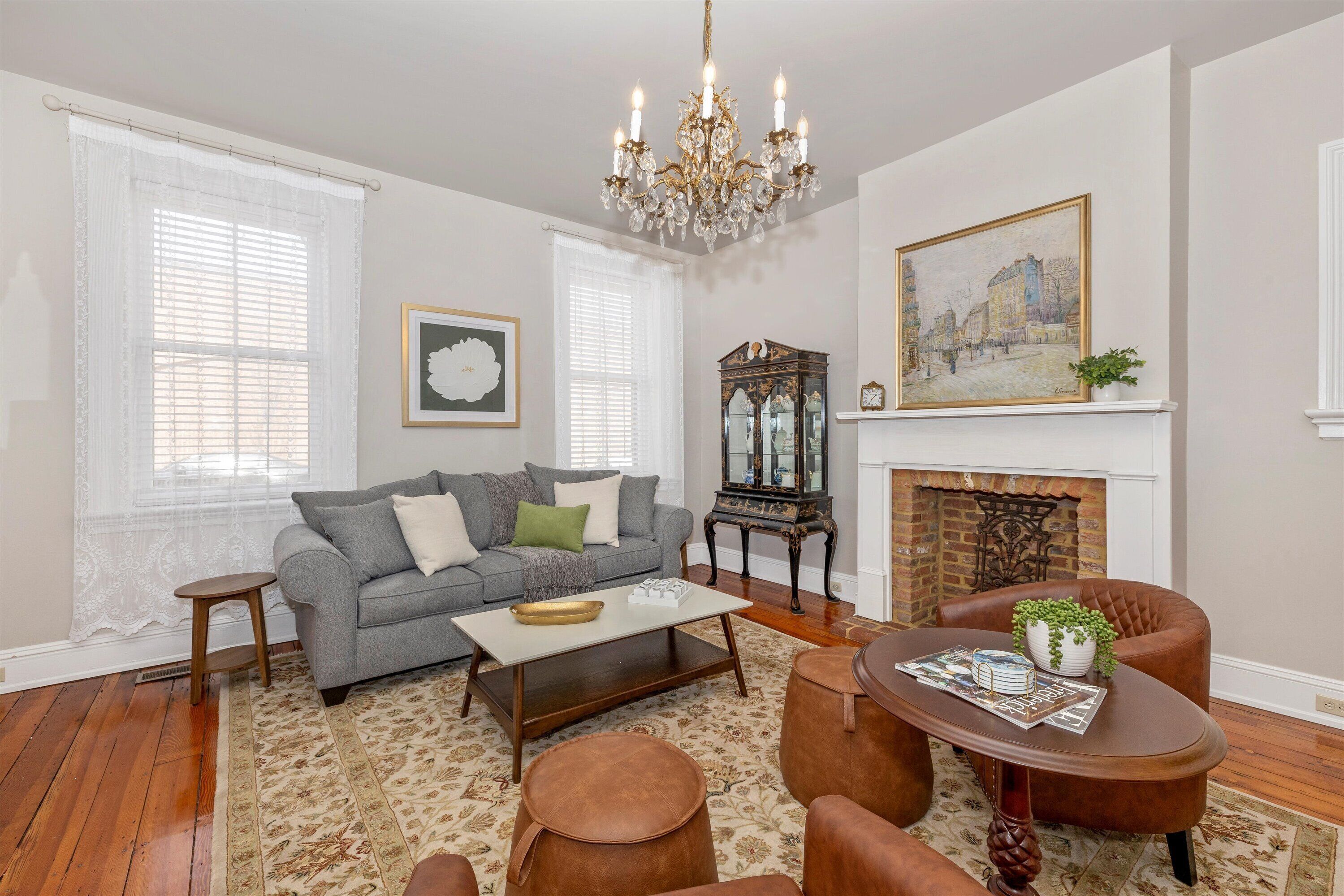 A living room with a fireplace, a chandelier, a sofa, a coffee table, and a fireplace mantel with a painting.