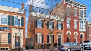 A red brick building with a black door and windows, a tree in front, and a parked car. - Gilded Age Getaway: Sleeps 6, free garage parking (Frederick)