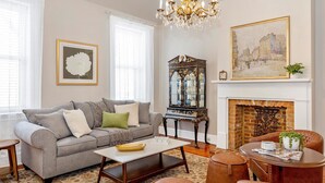 A living room with a grey sofa, a coffee table, a fireplace, and a chandelier. - Gilded Age Getaway: Sleeps 6, free garage parking (Frederick)