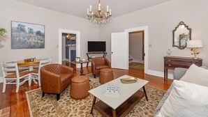 A living room with a chandelier, a dining area with a table and chairs, a television, and a large painting on the wall. - Gilded Age Getaway: Sleeps 6, free garage parking (Frederick)