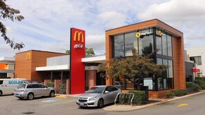McDonald’s-ravintola, jossa on leikkialueen kyltti, parkkipaikka autoineen ja tiiliverhoiltu julkisivu.