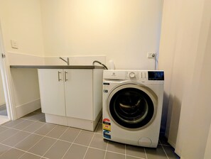 A compact laundry room with a front-loading washing machine, a small cabinet, and a tiled floor.